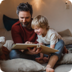 A father reads to his smiling young son.  